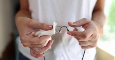 Woman wipes glasses with white napkin. Care of eyeglass frames for vision and ophthalmology