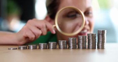 Woman is looking through magnifying glass at stack of coins. Financial analysis and verification of investment growth