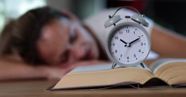 Tired female student at workplace in room took nap on bed with alarm clock. Sleepy freelancer resting while studying after sleepless night