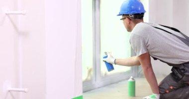 Boyacı, beyaz sprey boyayla pencere yamacını boyuyor. Pencere çerçevelerinin onarımı ve boyaması