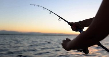 Hands of woman holding fishing rod in hands sea at sunset. Woman tourist fishing in sea or river