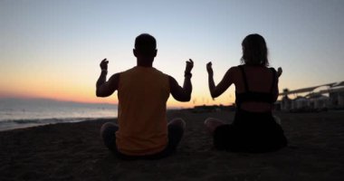 Two meditating at sunset sitting on the beach, back view. Yoga pose, relaxation on vacation, golden hour