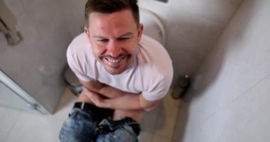 A smiling man sits on the toilet, slowmotion. Defecation problems, male health, shallow focus