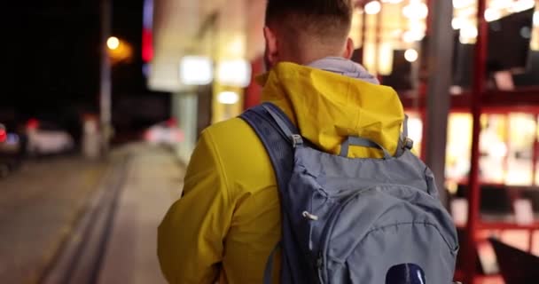 黄色のジャケットの男は 夕方の街の通り クローズアップ バックビューに沿って行く 街を歩く ショップウィンドウ — ストック動画