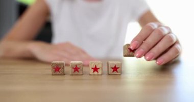 On the table in a row, wooden cubes are 5 stars, closeup, shallow focus. Woman adds a status, quality mark
