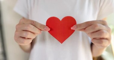 Young female hands hold a red paper heart, a close-up. Concept recognition of love, affection and friendship