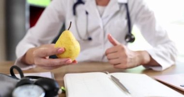 Young female hands of the doctor hold the fruit and show the gesture to the finger up, close-up. Concept Vitamin diet