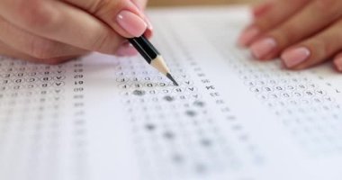 Macro female hands mark educational test options with a pencil, slowmotion. Multiple choice question, close-up