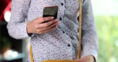 A girl in a shirt puts a smartphone in a leather purse, close-up. Woman with a bag and phone in the office
