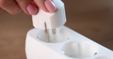 Female hands include white electric plug in a socket, close-up, slowmotion. Electricity interruptions, blackout