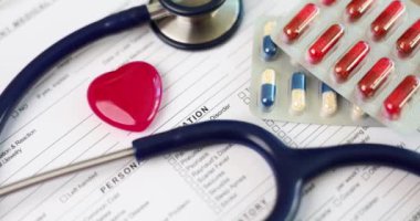 Red toy heart and stethoscope lying on medical documents with medicines closeup 4k movie slow motion. Treatment of diseases of cardiovascular system concept