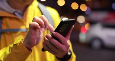 Male courier looking for information in mobile phone via internet on street at night closeup 4k movie slow motion. Fast delivery around clock concept