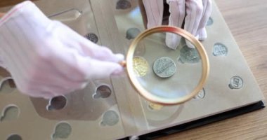 Numismatist examining old coin with magnifying glass closeup 4k movie slow motion. Hobby numismatics concept