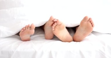 Male and female legs lying under covers in bed and stroking each other closeup 4k movie slow motion. Foreplay in sex concept