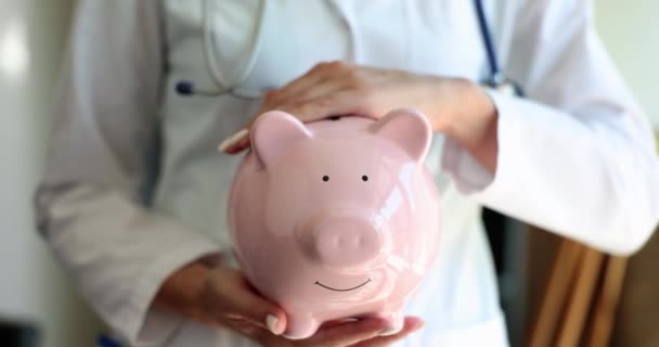Doctor Stroking Pink Piggy Bank Coins Closeup Movie Slow Motion — Stock video