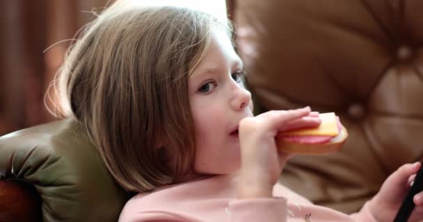 ソファに横になり チーズとソーセージとサンドイッチを食べる小さな女の子4K映画スローモーション 子供のためのスナックコンセプト — ストック動画
