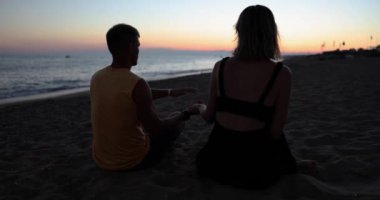 Couple in love sits on beach at sunset. Silhouette of couple in love holding hands