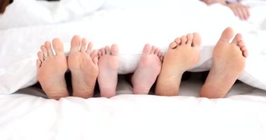 Cheerful mother father and child lie on the bed with white sheets. Comfortable calm relaxed family sleep
