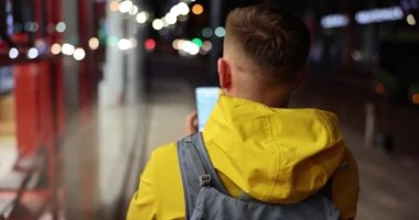 Erkek blogcu gezgin turist akşamları telefondan caddeye doğru yürür. Seyahat programınız için konum ve uygulamaları bulun