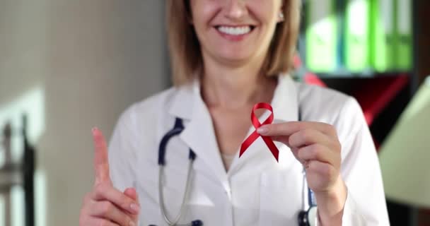 医師の手は赤いエイズ意識リボンと親指を持っています 男性と女性の兆候や症状や段階での注意エイズ — ストック動画
