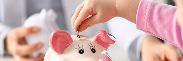 Child hand put a money coin in piggy bank to save money wealth. Family health insurance and budget