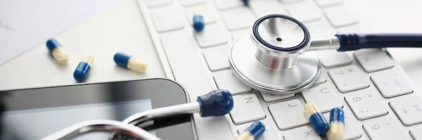 Tablets and stethoscope on computer keyboard closeup. Ordering medical pills drugs online on Internet