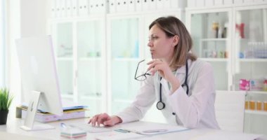 Düşünceli kadın doktor terapist klinikteki bilgisayar ekranına bakıyor. Uzaktan çevrimiçi hasta danışmanlığı veya eğitimi
