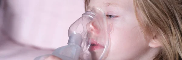 Sick girl in oxygen mask lies on hospital bed. Closeup portrait of child breathing in oxygen mask and lying in bed in pediatric ward