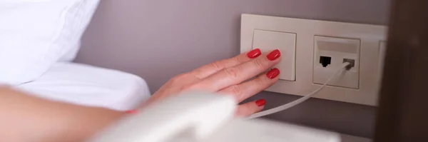 Woman hand turns off or turns on light with white switch closeup. Person person on power switch