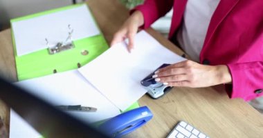 Businesswoman or secretary punching holes with hole puncher in documents in office. Business documentation archive