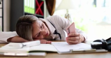 Tired female doctor at desk holding smartphone. Overwork negative emotions and waiting for calls in clinic of doctor
