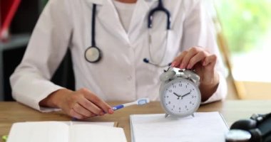 Dentist holding toothbrush and alarm clock in hands. Time to brush teeth properly