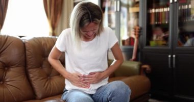 Woman sitting on couch with severe abdominal pain touching stomach. Abdominal pain and menstrual pain