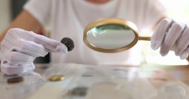 Person holding old silver coin and magnifying glass. Numismatics and coin valuation