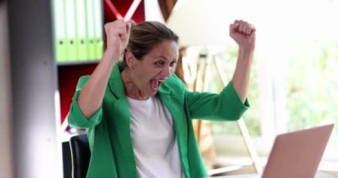 Excited businesswoman sits at a computer and feels euphoric. Woman winning online lottery or good online news