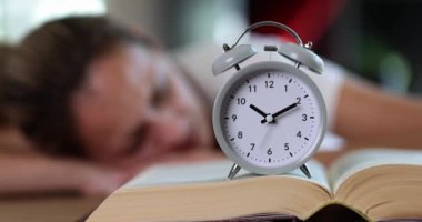 Woman sleeps with alarm clock and book. Fatigue overwork and preparation for exams