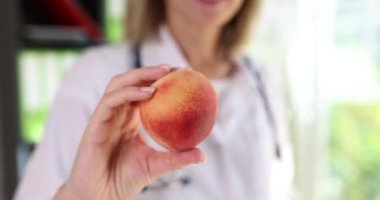 Doctor nutritionist holds juicy tasty peach in clinic. Instruct patient to eat healthy