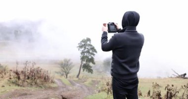 Silhouette of blogger photographer taking photo in front of misty mountains. Traveler taking pictures of mountains and natural landscape