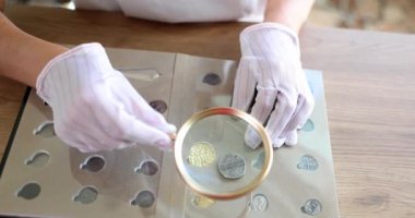 Numismatist examines coin from collection through magnifying glass. Studying history of coinage