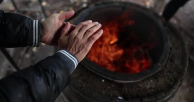 Male hands of are warming themselves by fire of barrel in dark. Homeless person or tourist in nature