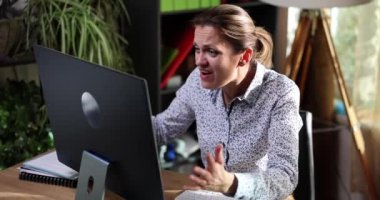 Angry business woman screaming into computer monitor at workplace. Negative emotions bad business news