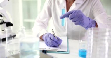 Doktor mavi sıvıyla test tüpünü tutuyor ve kimyasal rapor yazıyor. Zehirli maddelerin laboratuvar analizi