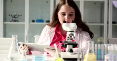 Young female scientist using microscope touchpad in laboratory. Microscope and microscopic research methods