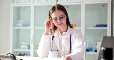 Tired female doctor sitting at table and holding glasses in clinic. Overtime work and fatigue of doctors