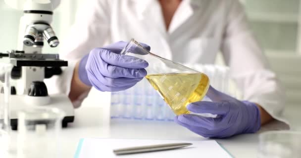 研究室での医療生産と油制御 科学者は手に金の液体でフラスコを保持し 工場で最終製品の品質の検査を行います — ストック動画