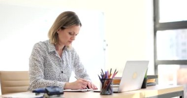 Thoughtful woman plans work schedule and writes in notebook. Woman administrative manager takes notes about viewed information