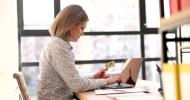 Woman manager holding credit card while making online payment. Woman holding debit card in hands and using laptop to shop online