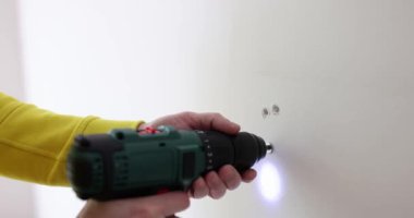 Worker makes hole in white wall with drill. Handyman working on construction site
