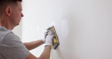 Male master builder finisher polishes the wall with sandpaper. Painting, plastering and interior decoration