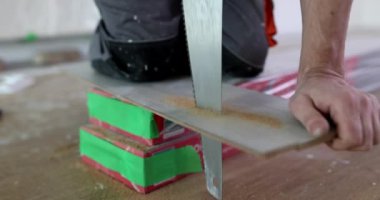 Worker cuts piece of laminate with hand saw. Cutting flooring with hand saw